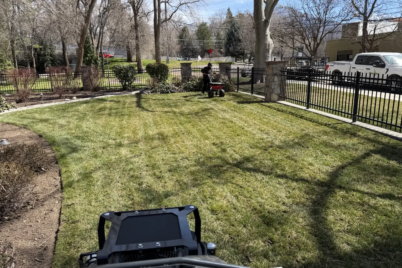 Green Lawn Utah crew aerating and spreading fertilizer on a fenced front lawn
