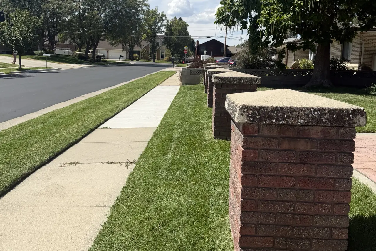 Trimmed park strip and lawn along a residential street with brick pillars